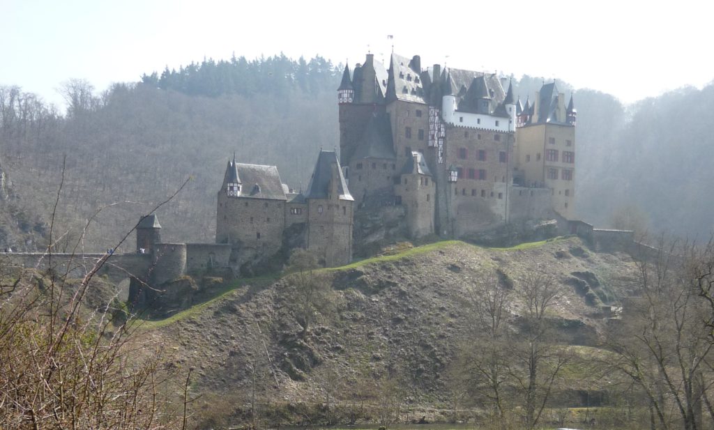 Stone castle on a hill, surrounded by the River Eltz and more hills, near the Mosel valley in Germany.