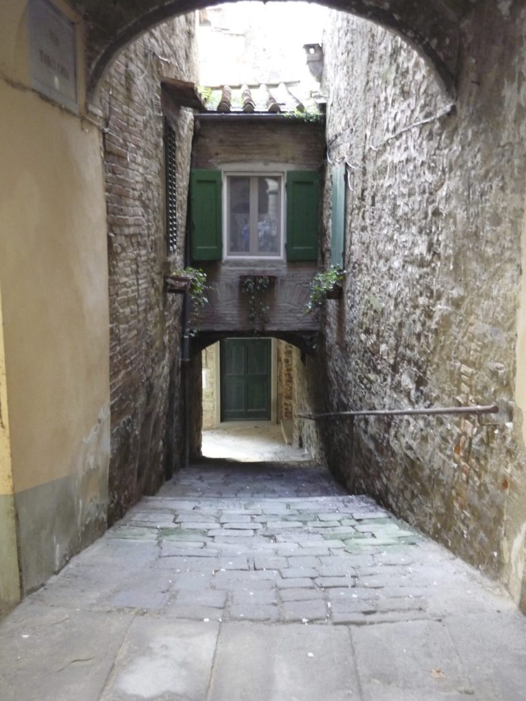 Alley leading to an archway with light shining behind it.