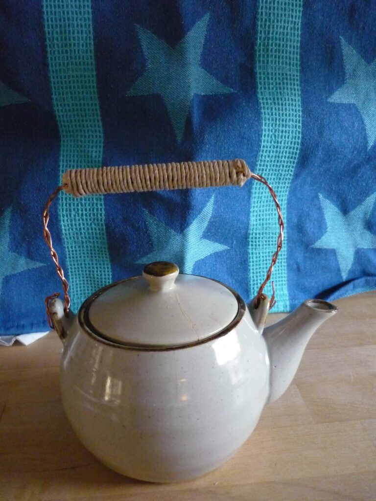 Teapot with new wire handle on a round beige teapot with a cracked lid.