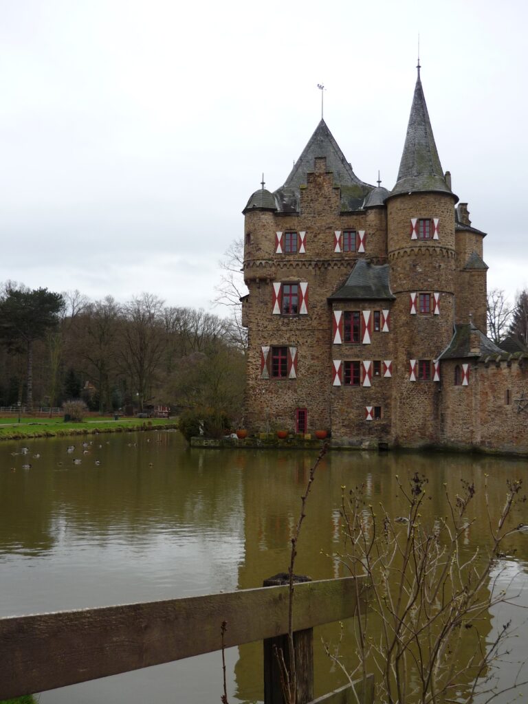 Castle with towers and moat and red and white patterned shutters. Burg Satzvey, Germany.