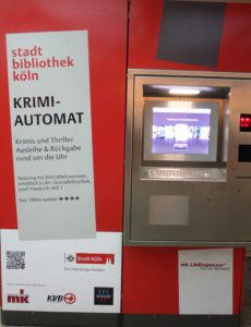 Vending machine for mystery novels from the city library in Cologne. Big red box with computer screen and door with window to get book.