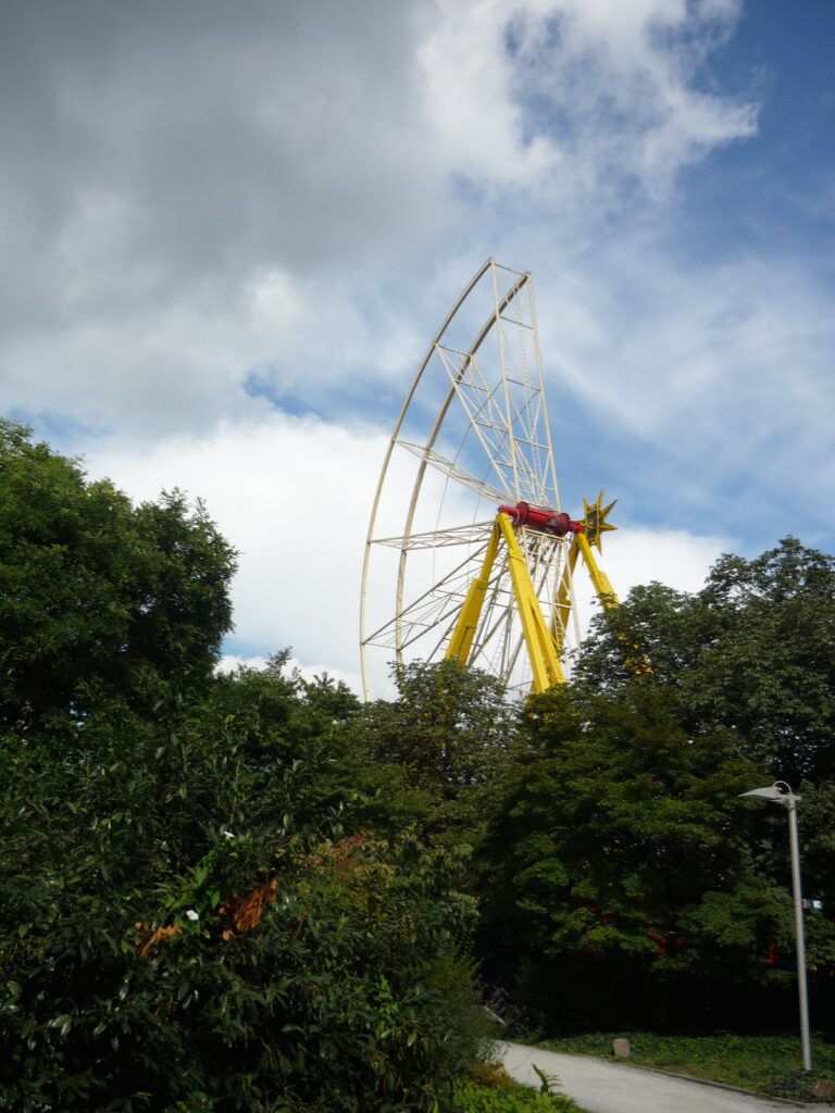 A partially constructed ferris wheel against a blue sky with puffy white clouds.