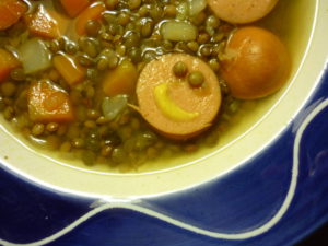 Lentil soup with a slice of hot dog that looks like a smiley face with a mustard smile and two lentil eyes.