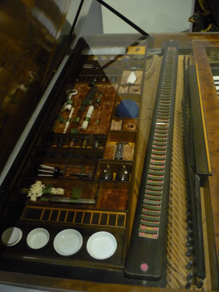 photo of compartments under the lid of a piano, paintboxes, brushes, sewing things