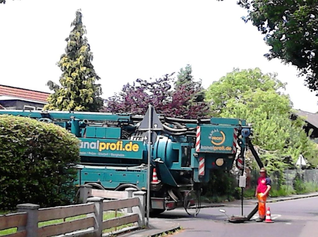 Massive green sewer truck and man in orange reflective clothing.