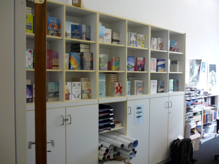 white bookcase with square cubbies to hold stacks and display standing up copies of new books, some shrink-wrapped