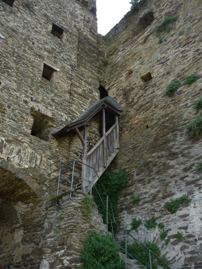 Stone castle walls with skinny steep wooden staircase (half-covered with wooden roof)