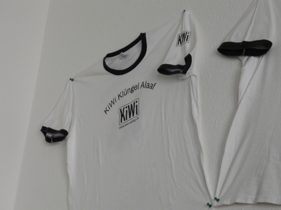 White t-shirt with Kiwi logo pinned to wall.