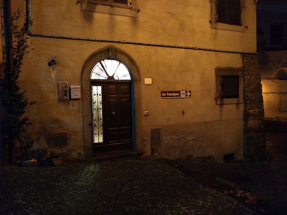 lit doorway on a dark house with Via Francigena sign